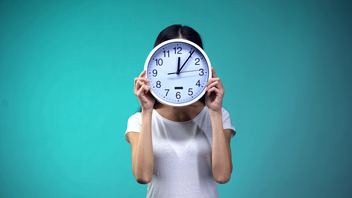 Woman holding big clock before her face, time management and routine, deadline